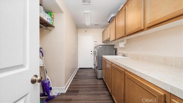 clothes washing area featuring washing machine and clothes dryer, baseboards, dark wood finished floors, cabinet space, and a sink