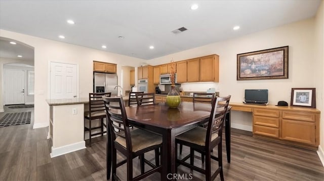 dining area with dark wood-style floors, visible vents, recessed lighting, arched walkways, and built in desk