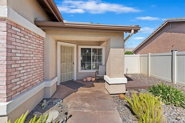 doorway to property with brick siding, fence, a patio, and stucco siding