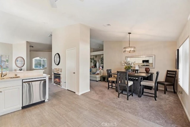 dining room featuring a chandelier, light colored carpet, a fireplace, visible vents, and vaulted ceiling