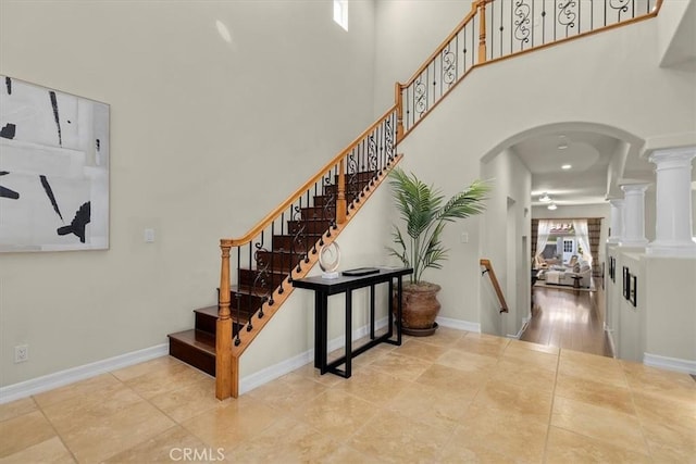 staircase featuring decorative columns, arched walkways, a high ceiling, and baseboards