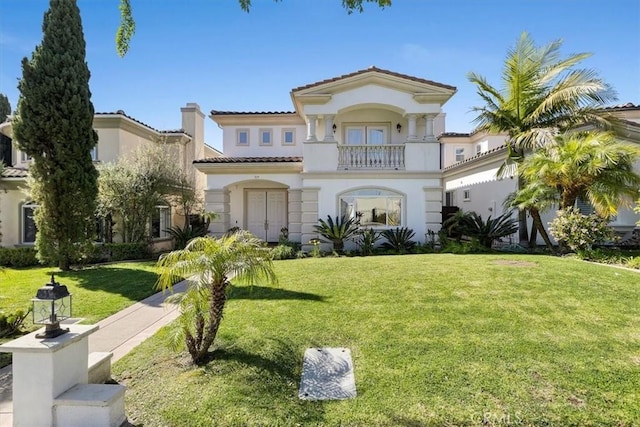 mediterranean / spanish-style house with a tiled roof, a front yard, a balcony, and stucco siding