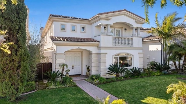 mediterranean / spanish house with a balcony, fence, a tile roof, stucco siding, and a front yard