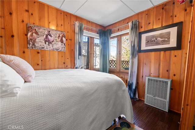 bedroom with wooden walls, dark wood-style flooring, and heating unit