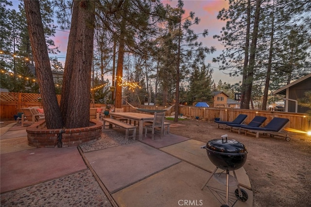 patio terrace at dusk featuring a fenced backyard, a fire pit, and outdoor dining area