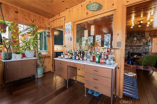 bar featuring a stone fireplace, wood walls, dark wood finished floors, and wood ceiling