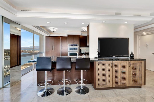 kitchen featuring dark brown cabinets, expansive windows, a kitchen bar, double oven, and modern cabinets