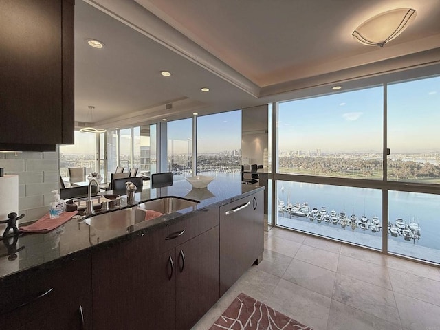 kitchen featuring floor to ceiling windows, dark stone countertops, a water view, and a sink