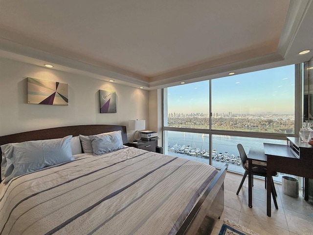 bedroom featuring a water view, a tray ceiling, expansive windows, light tile patterned floors, and a view of city