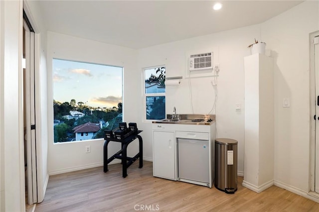 kitchen with baseboards, a wall mounted AC, light wood-style flooring, a sink, and white cabinets