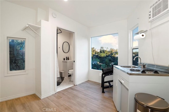 clothes washing area with a sink, baseboards, an AC wall unit, and light wood-style flooring