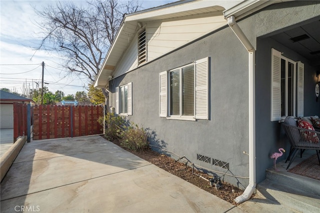 view of property exterior with crawl space, stucco siding, fence, and a patio