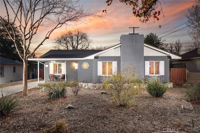 view of front facade with a chimney, fence, and stucco siding