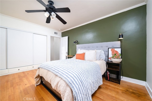 bedroom with ceiling fan, light wood-style flooring, baseboards, ornamental molding, and a closet