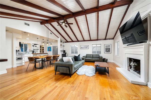 living room featuring light wood finished floors, ceiling fan, a fireplace, and visible vents