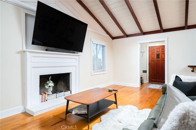 living room featuring lofted ceiling with beams, a fireplace with raised hearth, baseboards, and light wood-style floors