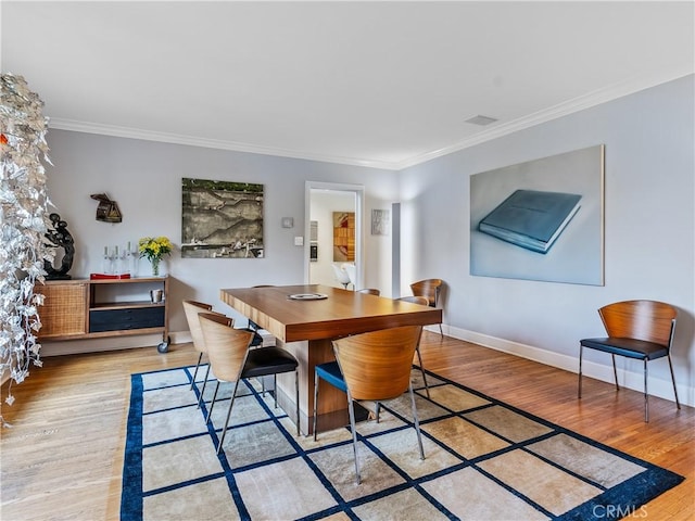 dining area featuring ornamental molding, light wood-style flooring, and baseboards