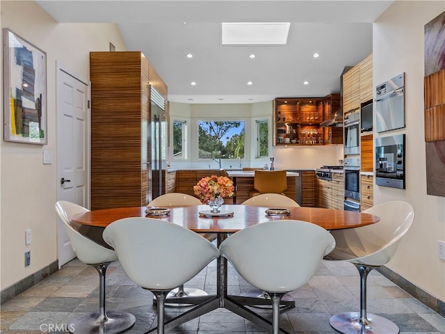 dining space featuring a skylight, stone finish flooring, baseboards, and recessed lighting