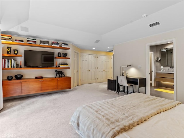 bedroom featuring connected bathroom, light colored carpet, visible vents, multiple closets, and a tray ceiling