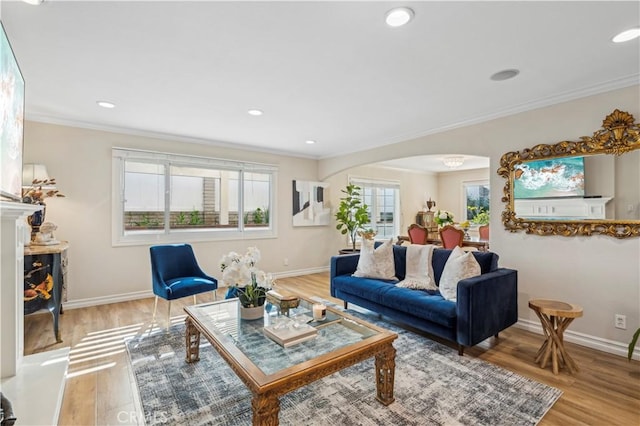 living area with baseboards, crown molding, arched walkways, and wood finished floors