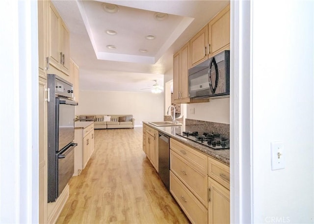 kitchen with a tray ceiling, open floor plan, a sink, light wood-type flooring, and black appliances