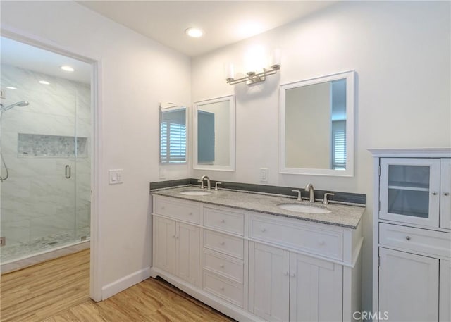 bathroom featuring double vanity, a stall shower, a sink, and wood finished floors