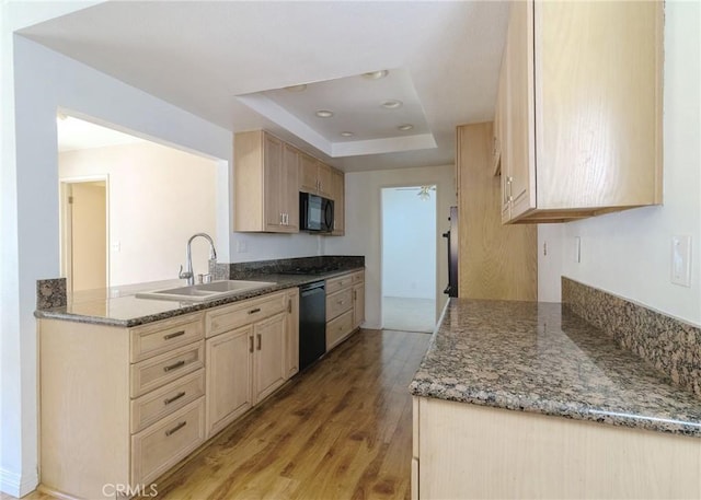 kitchen featuring a raised ceiling, light wood-style flooring, black appliances, light brown cabinets, and a sink