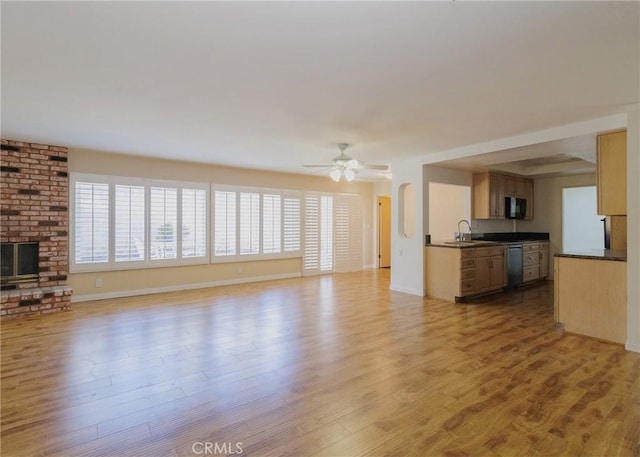 unfurnished living room with baseboards, a ceiling fan, light wood-type flooring, a brick fireplace, and a sink