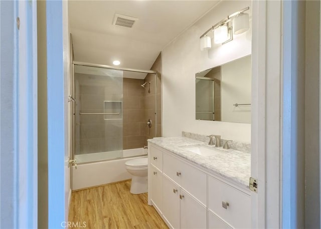 bathroom with visible vents, toilet, enclosed tub / shower combo, wood finished floors, and vanity