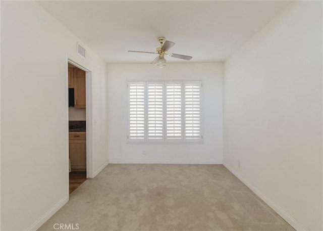 unfurnished room featuring baseboards, visible vents, a ceiling fan, and light colored carpet