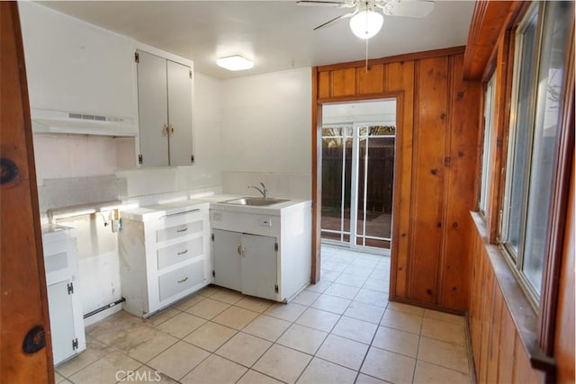 kitchen with light countertops, white cabinetry, wood walls, a sink, and under cabinet range hood