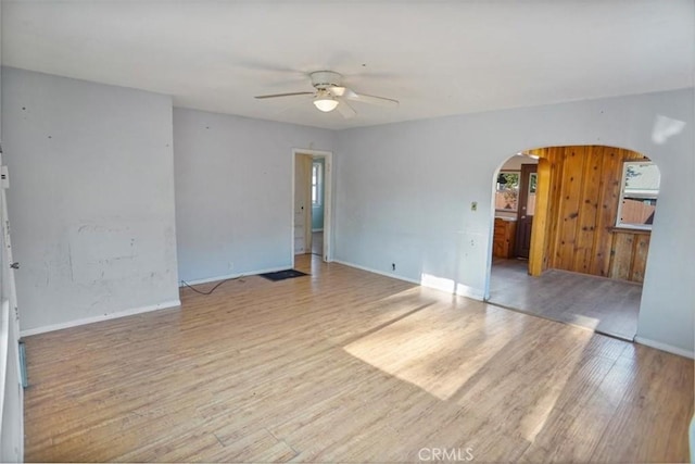 unfurnished room with arched walkways, light wood-type flooring, a ceiling fan, and baseboards