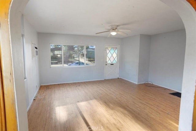 spare room featuring light wood-style floors, arched walkways, baseboards, and a ceiling fan