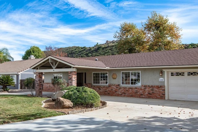 single story home featuring an attached garage, brick siding, roof with shingles, stucco siding, and a front yard