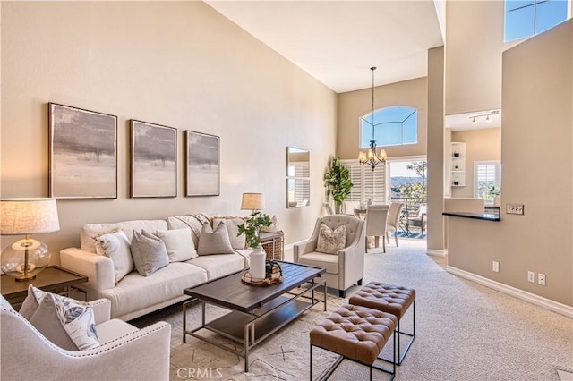 living room with a high ceiling, light colored carpet, baseboards, and an inviting chandelier