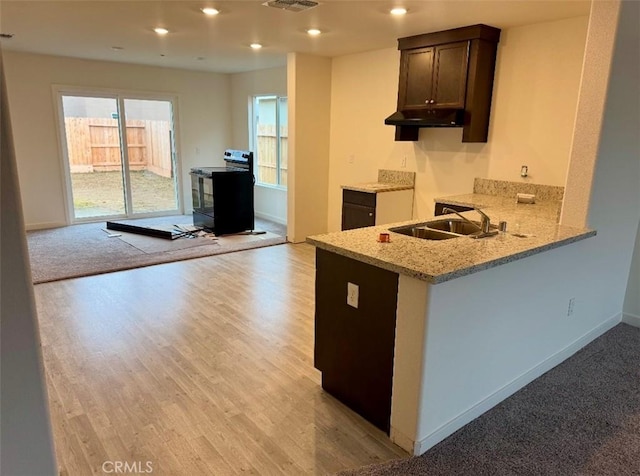 kitchen with black range with electric stovetop, dark brown cabinetry, a sink, light stone countertops, and under cabinet range hood