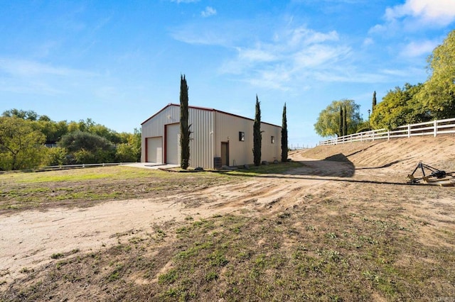 exterior space with a detached garage, dirt driveway, fence, a pole building, and an outdoor structure