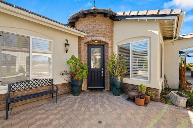 doorway to property featuring stone siding, a patio area, and stucco siding