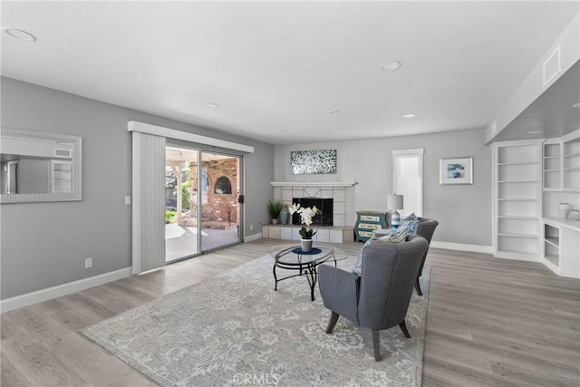 living room with light wood-type flooring, a fireplace, visible vents, and baseboards