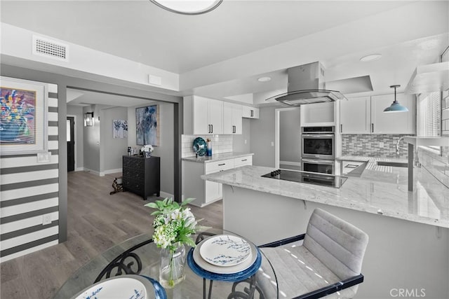 kitchen with hanging light fixtures, island range hood, white cabinetry, and double oven