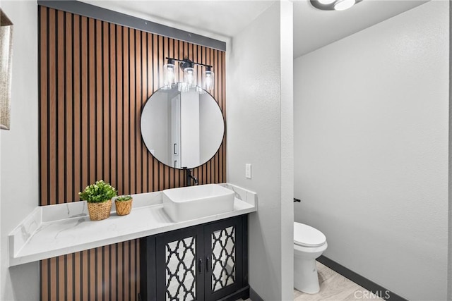 half bathroom with toilet, wood finished floors, and vanity