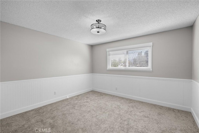 unfurnished room with light carpet, a wainscoted wall, and a textured ceiling