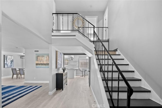 stairway with a towering ceiling, wood finished floors, visible vents, and baseboards