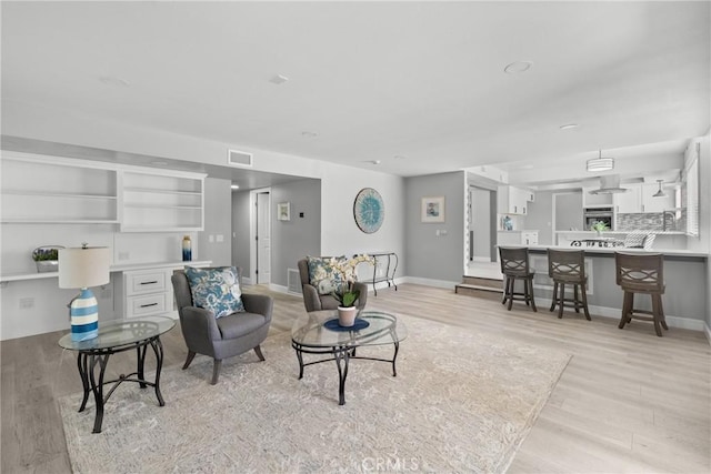 living area with light wood-style flooring, visible vents, and baseboards