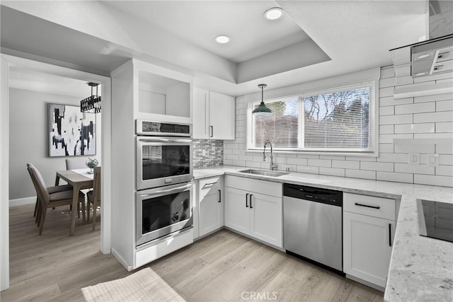 kitchen with light wood finished floors, stainless steel appliances, hanging light fixtures, white cabinets, and a sink