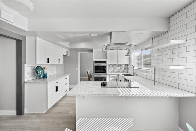 kitchen with black electric stovetop, a peninsula, a sink, white cabinetry, and island exhaust hood