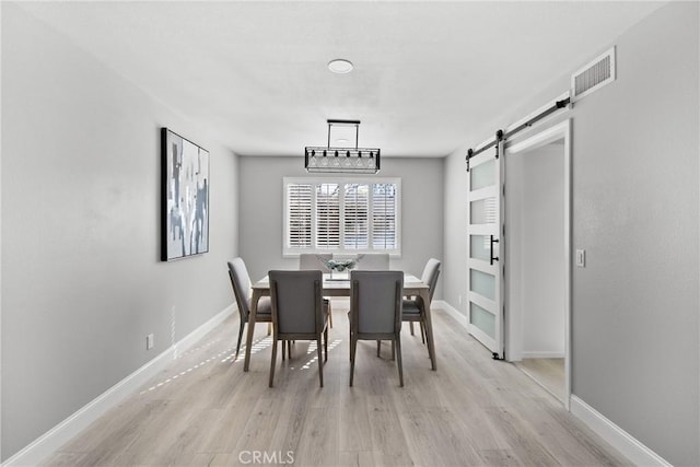 dining area featuring light wood finished floors, a barn door, visible vents, and baseboards