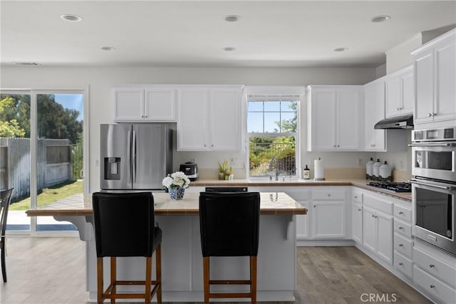 kitchen with under cabinet range hood, stainless steel appliances, a breakfast bar, a sink, and white cabinets