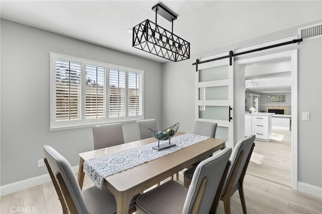 dining area featuring visible vents, a barn door, light wood-style flooring, and baseboards