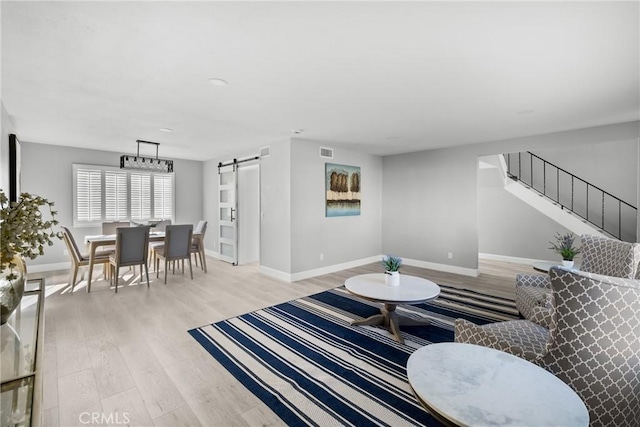 living area with visible vents, light wood-style flooring, a barn door, baseboards, and stairs